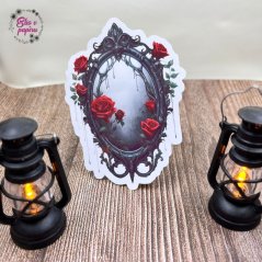 Gotické zrcadlo zdobené černými ornamenty, z něhož kapou tmavé stíny. Okolo něj jsou rozesety červené růže, které přidávají dramatický kontrast.